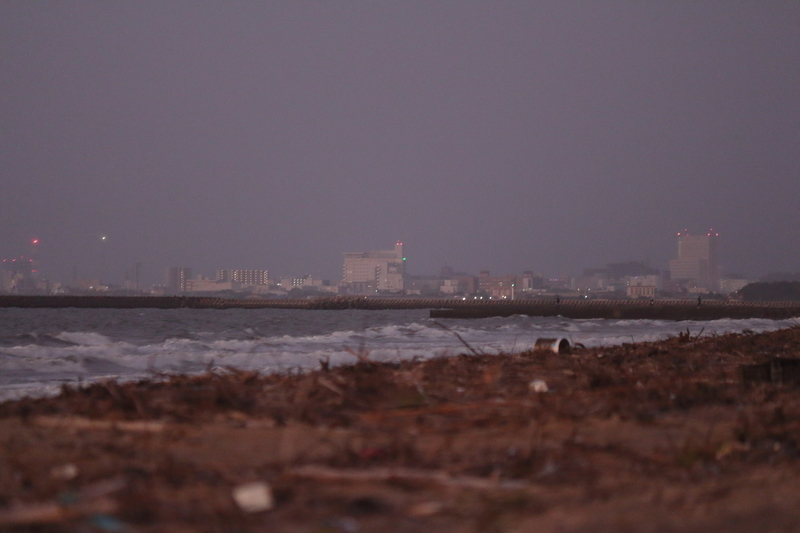 台風が過ぎ去った後の伊勢湾の海岸の風景を撮影した写真④少し荒れ気味の海の向こうに朝の市街地が見えている。