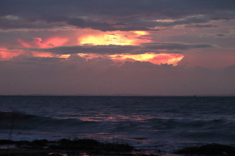 海と朝焼けの空を撮影した画像①灰色の雲の合間から真っ赤な朝焼けの空が見える。